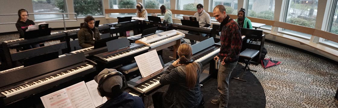 Music instructor Ben Thomas talking with students in piano class.